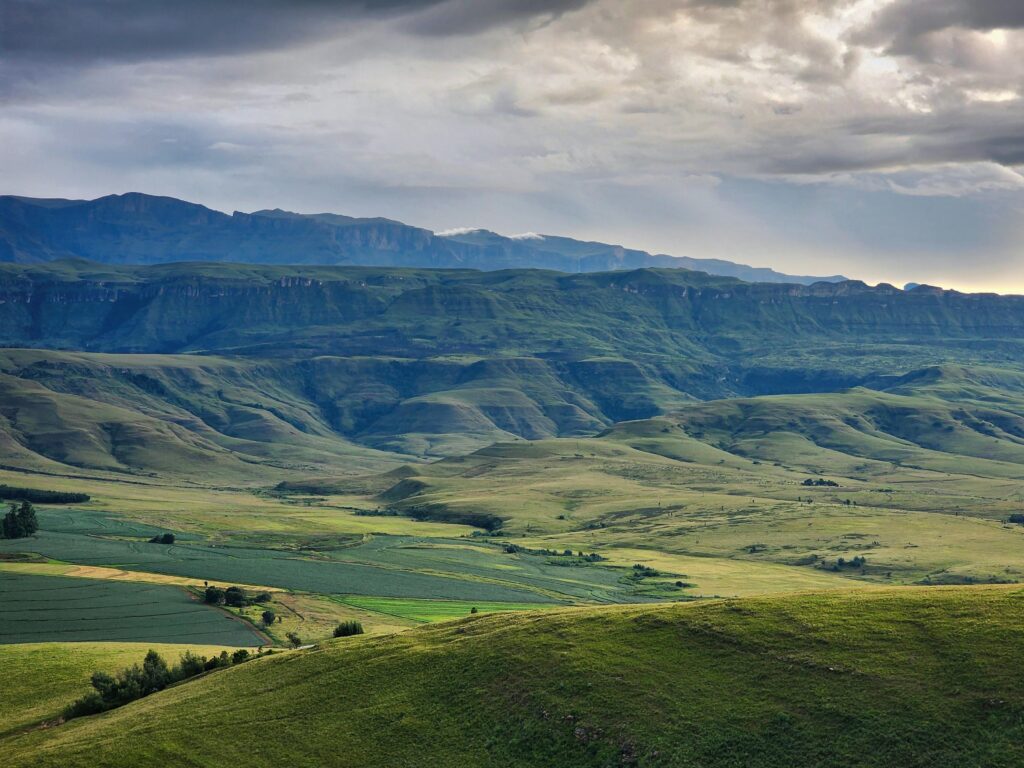 Breathtaking landscape of the Drakensberg mountains with lush greenery and dramatic cloudy sky.