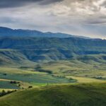 Breathtaking landscape of the Drakensberg mountains with lush greenery and dramatic cloudy sky.