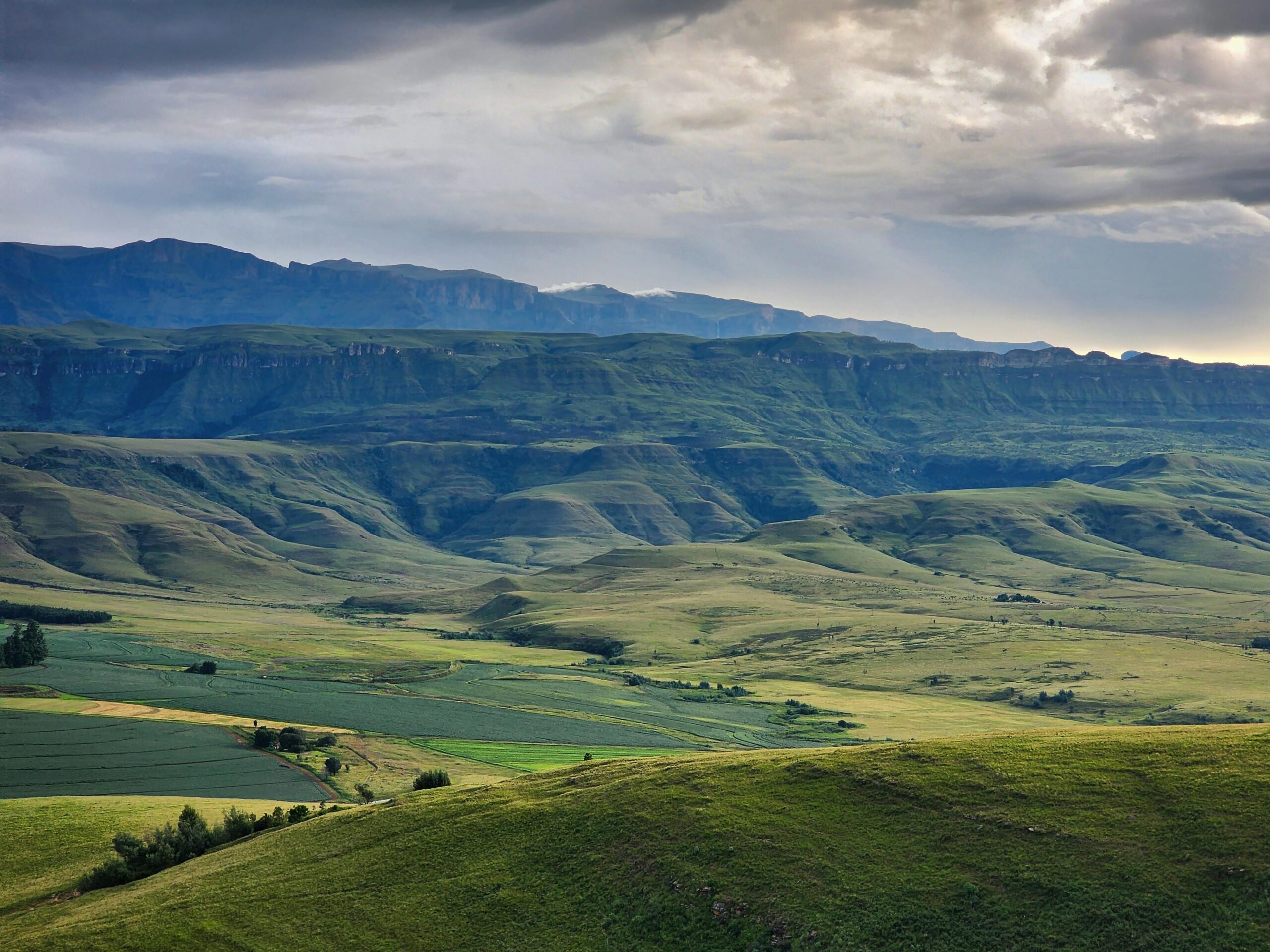 Breathtaking landscape of the Drakensberg mountains with lush greenery and dramatic cloudy sky.
